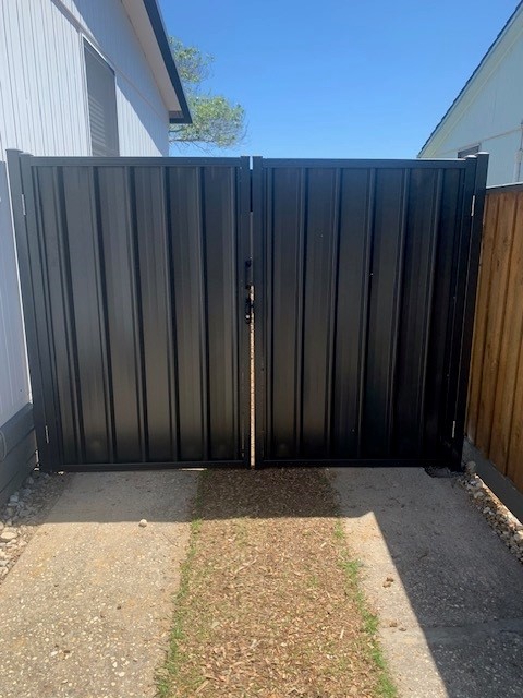 Trimclad double gate in dark Colorbond steel fitted between a house wall and timber fence over a concrete driveway