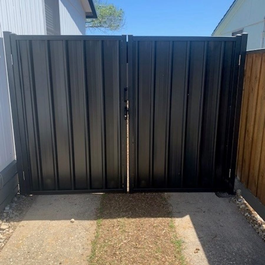 Trimclad double gate in dark Colorbond steel fitted between a house wall and timber fence over a concrete driveway