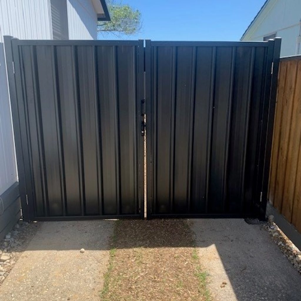 Trimclad double gate in dark Colorbond steel fitted between a house wall and timber fence over a concrete driveway